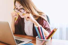 Junge Frau hinter einem Laptop. Auf einen Bleistift beißend