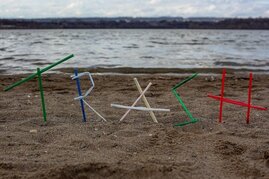 Schriftzug "Trash" aus Strohhalmen am Strand - mit Blick auf das Meer