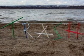 Schriftzug "Trash" aus Strohhalmen am Strand - mit Blick auf das Meer