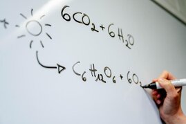 Eine Hand schreibt chemische Formeln auf eine Tafel