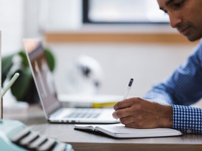 Schreibtisch mit Laptop; Person angeschnitten