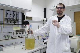 Doktorand Dragan Trifunovic mit einer großen Flasche und einem kleinen Reagenzglas, die kultivierte Thermotoga maritima-Bakterien