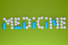 Schriftzug "Meicine" gelegt aus runden weißen Tabletten udn blauen Kapslen auf grünem Grund