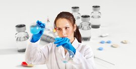 Laborantin im Labor füllt blaue Flüssigkeit in Standkolben