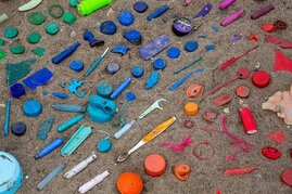 verschiedene Plastikgegenstände auf Sand - sortiert nach Regenbogenfarben