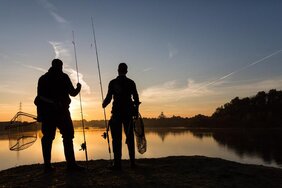 Sonnenuntergnag mit Silhouette von zwei Anglern vor einem See
