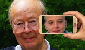 Alter Mann hinten - im Vordergrund Smartphone mit Kindergesciht
